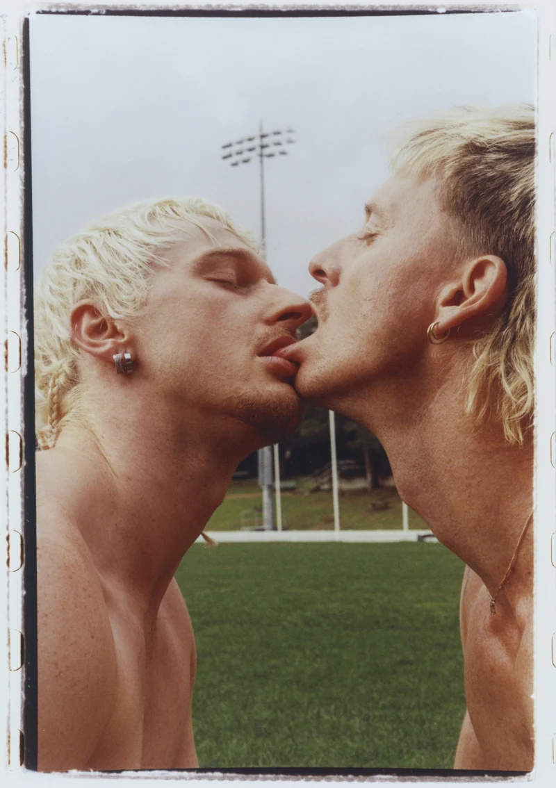 Two men face each other, their lips almost touching, on a football field.